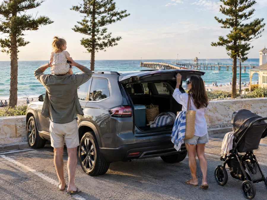 Family unpacking a grey SUV at a Perth beach car park with the jetty behind them